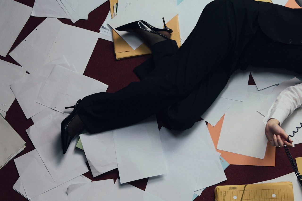 Editorial flat lay of scattered documents and black heels on a deep red floor